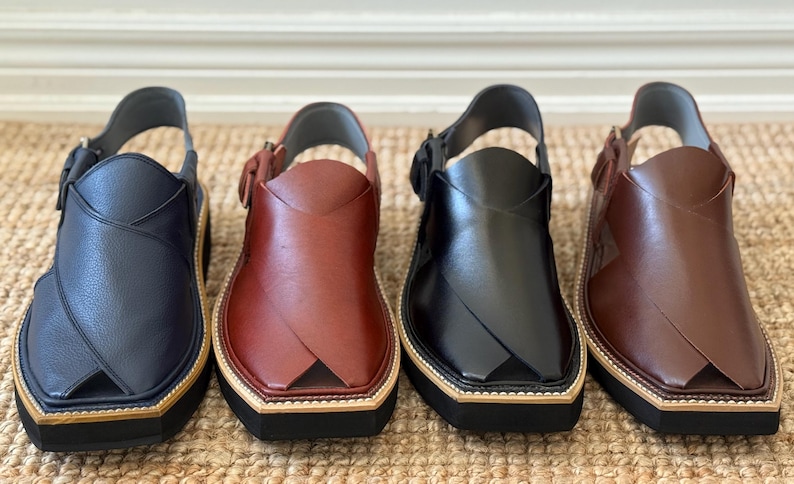 May include: Four pairs of leather Peshawari sandals in navy blue, burgundy, black, and brown. Each sandal features a strap, a buckle, and a thick sole with a light-coloured trim.