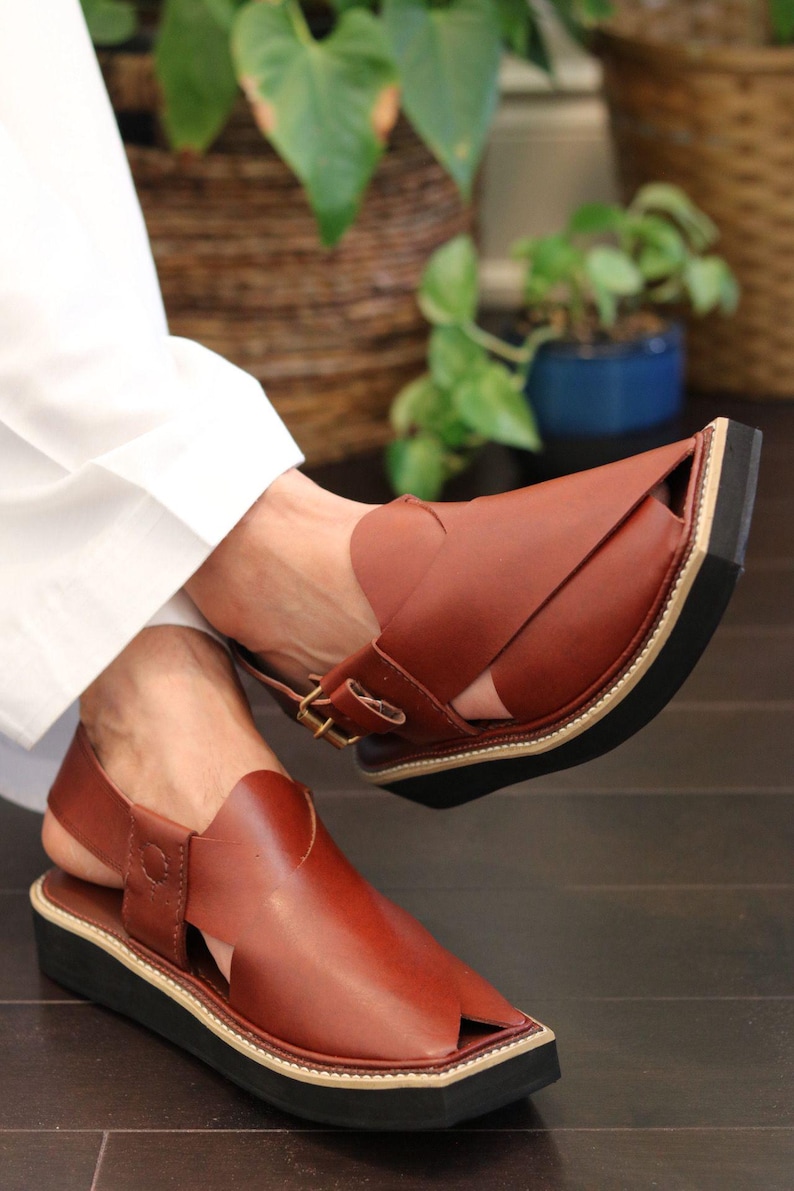 May include: Brown leather sandals with a black sole and a beige trim. The sandals have a strap that goes around the ankle and a buckle closure. The sandals are a traditional style.