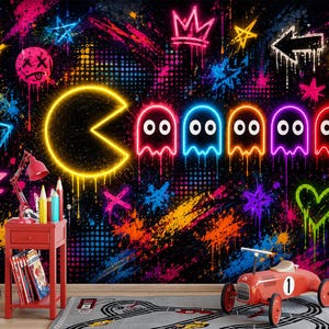 Könnte beinhalten: Ein Wandbild mit einem gelben Pac-Man im Neon-Stil und fünf bunten Geistern vor einem schwarzen Hintergrund mit lebhaften Graffiti, Farbspritzern, Kronen, Sternen und einem Smiley. Ein roter Beistelltisch, ein rotes Spielzeugauto und ein Wegweiser.