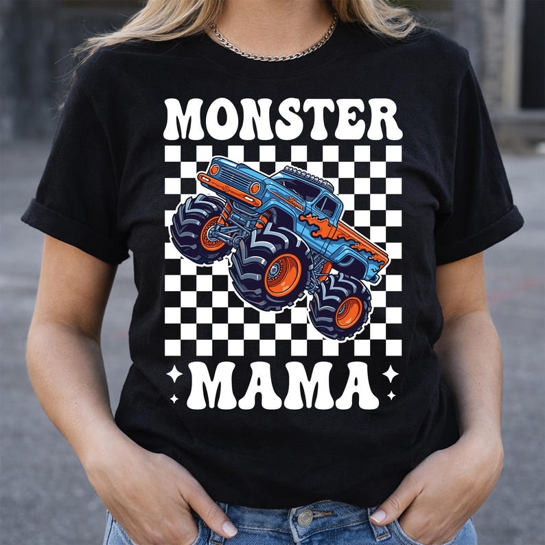 Op de afbeelding: Zwart T-shirt met een blauw en oranje monster truck ontwerp op een geruite achtergrond. De tekst "MONSTER MAMA" staat in witte, gestileerde letters. Het ontwerp bevat vlammen en grote banden.