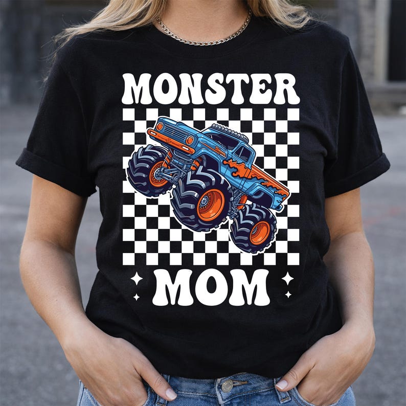 Puede incluir: Camiseta negra con un gr&aacute;fico de cami&oacute;n monstruo azul y naranja y las palabras "MONSTER MOM" en blanco. El dise&ntilde;o incluye un fondo a cuadros en blanco y negro. La camiseta es de manga corta.