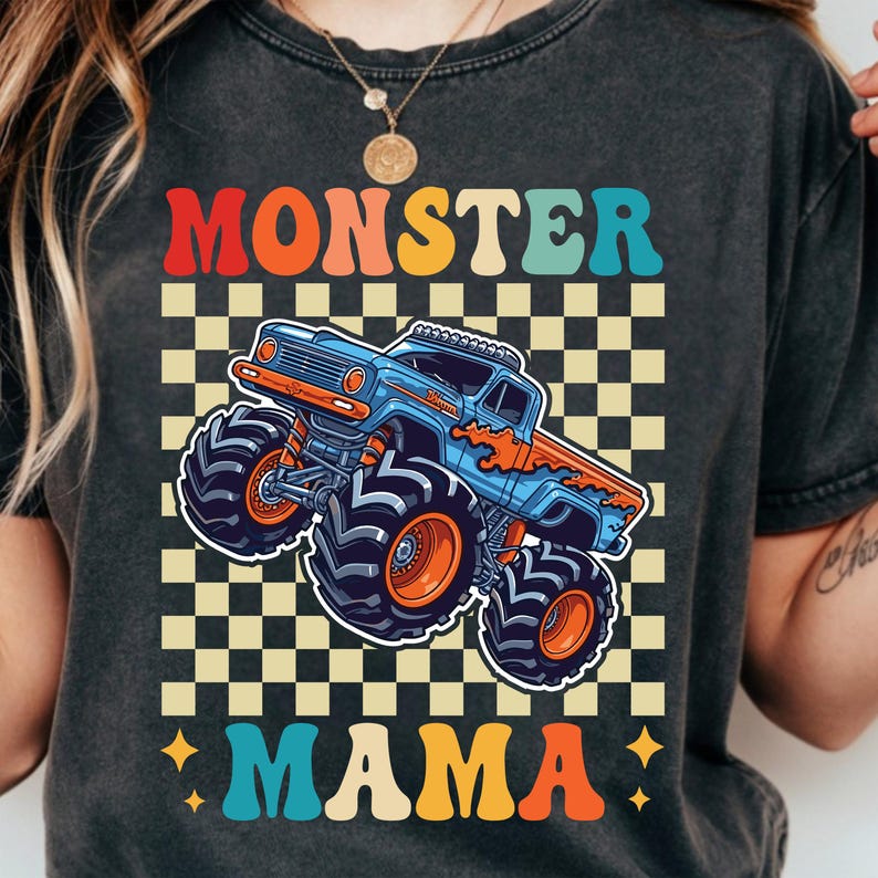 May include: Dark gray t-shirt with a colorful graphic of a blue and orange monster truck on a checkered background. The words "MONSTER MAMA" are printed above and below the truck in retro-style lettering.