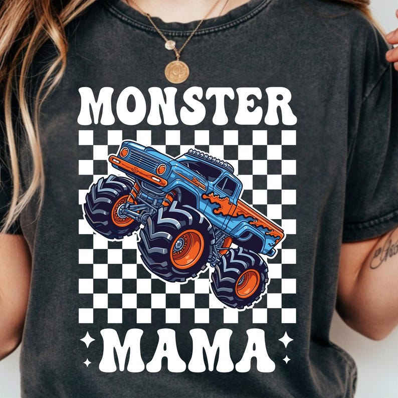 Op de afbeelding: Donkergrijs t-shirt met een blauw en oranje monster truck ontwerp op een zwart-wit geblokte achtergrond. De tekst "MONSTER MAMA" staat boven en onder de truck. De truck heeft grote banden.