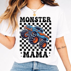 May include: White t-shirt featuring a blue and orange monster truck graphic with the words "MONSTER MAMA" in black. The design includes a black and white checkered background.