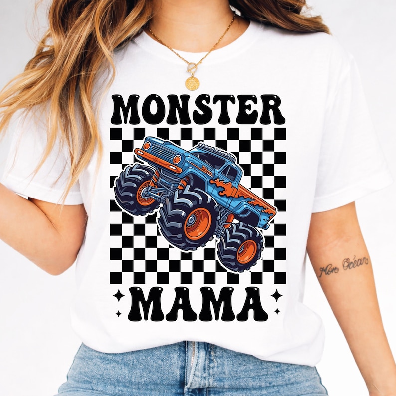 May include: White t-shirt featuring a blue and orange monster truck graphic with the words "MONSTER MAMA" in black. The design includes a black and white checkered background.