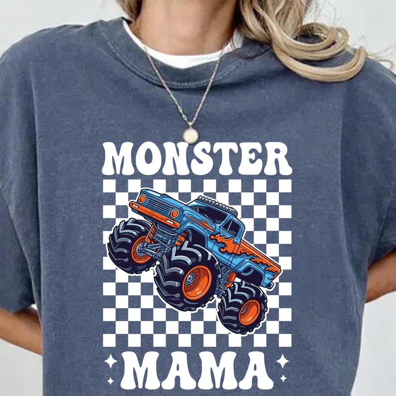 Op de afbeelding: Een marineblauw sweatshirt met een afbeelding van een blauwe en oranje monstertruck op een geruite achtergrond. De woorden "MONSTER MAMA" staan in het wit boven en onder de truck.