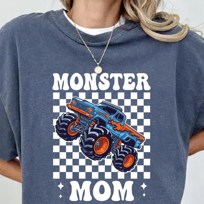 Puede incluir: Una sudadera azul marino con un gr&aacute;fico de un cami&oacute;n monstruo azul y naranja sobre un fondo a cuadros. Las palabras "MONSTER MOM" est&aacute;n impresas en letras blancas en la parte superior e inferior del cami&oacute;n.