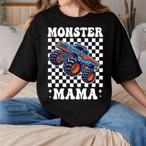 Op de afbeelding: Zwart T-shirt met een blauwe en oranje monstertruck op een geruite achtergrond. De woorden "MONSTER MAMA" zijn in het wit gedrukt, in een retro lettertype.