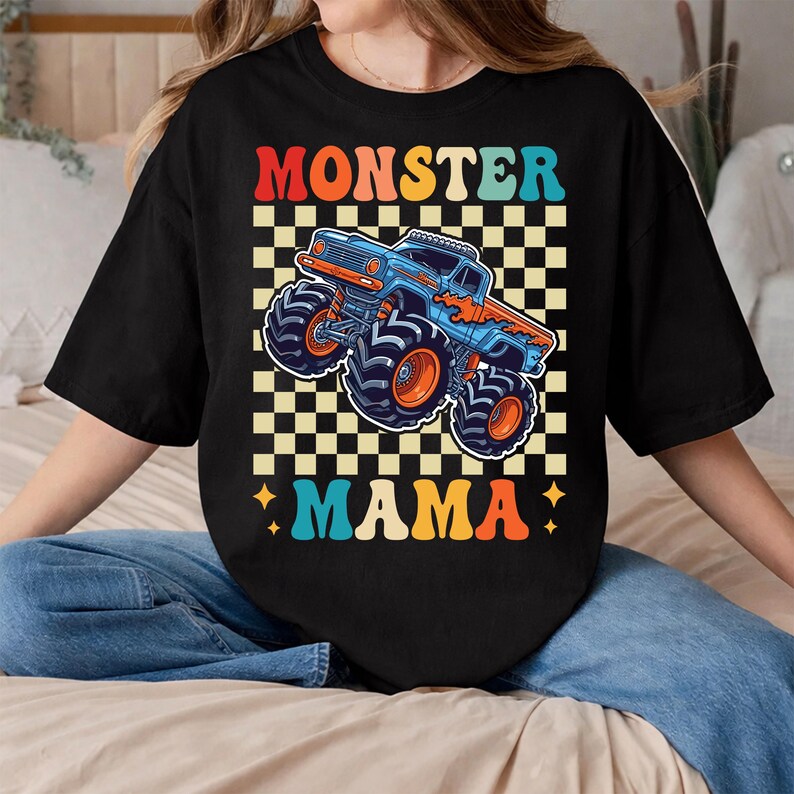 May include: Black t-shirt with a colorful graphic featuring a blue monster truck with orange flames and wheels. The text "MONSTER MAMA" is displayed in a retro font, set against a checkered background.