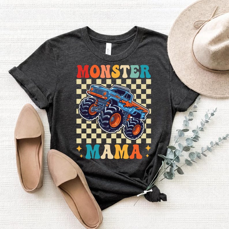 May include: Dark gray t-shirt with a colorful graphic of a blue monster truck with orange wheels and the words "MONSTER MAMA". The design is set against a black and white checkered background.