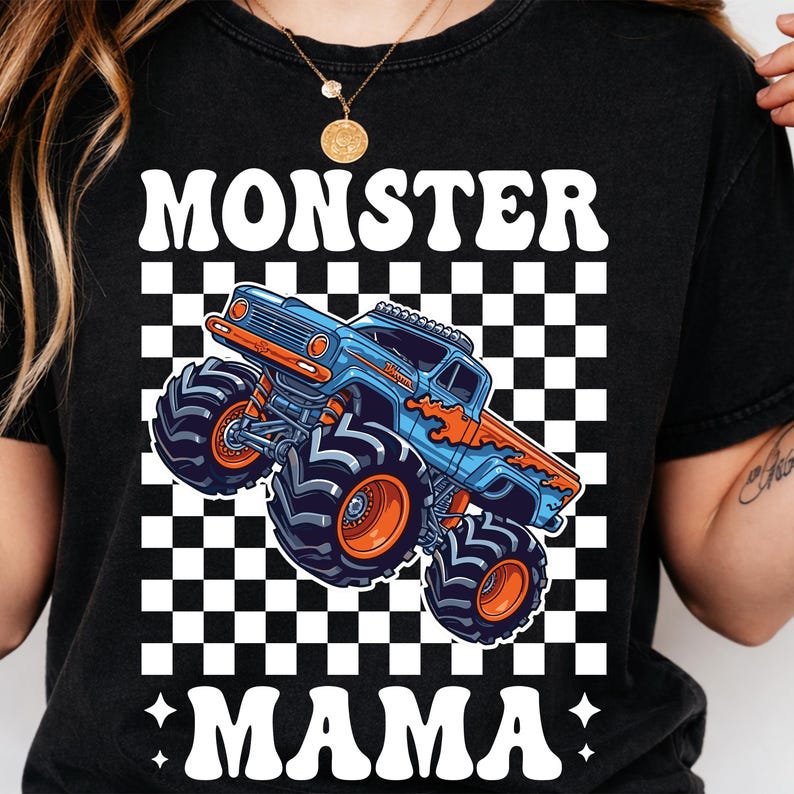 Op de afbeelding: Zwart T-shirt met een afbeelding van een blauwe en oranje monstertruck. De tekst "MONSTER MAMA" staat in het wit boven en onder de truck, tegen een zwart-witte geblokte achtergrond. Het shirt heeft een ronde hals.