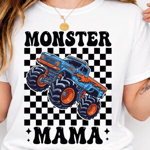 May include: White t-shirt featuring a blue and orange monster truck graphic with the text "MONSTER MAMA" in black. The design includes a checkered background.
