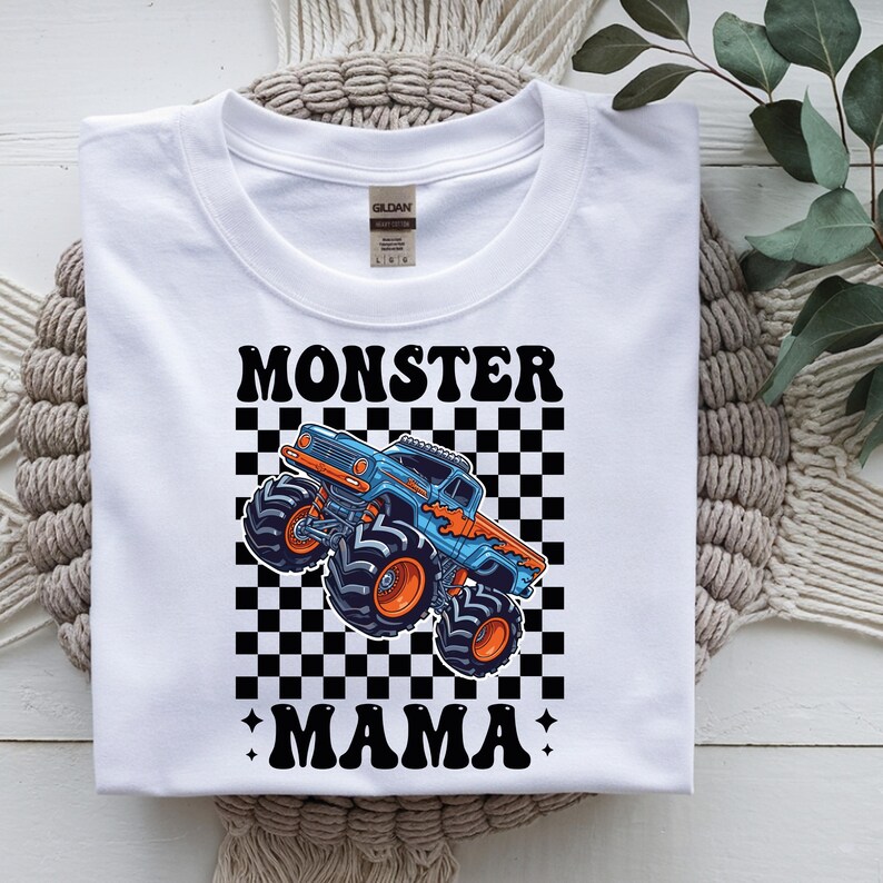 May include: White t-shirt with a graphic of a blue and orange monster truck on a black and white checkered background. The words "MONSTER MAMA" are printed above and below the truck in black.