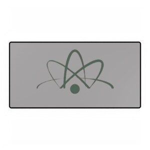 May include: A rectangular mouse mat with a grey surface and a black border. The mat features a green atom symbol design in the centre.
