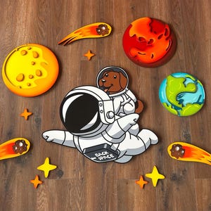 Peut inclure: Un ensemble sur le thème de l'espace avec un chien astronaute de dessin animé, des planètes, des étoiles et des comètes. L'astronaute porte une combinaison spatiale blanche avec le texte "BACK SPACE". Les planètes comprennent un soleil jaune, une planète rouge, une Terre bleue et verte et une lune grise.