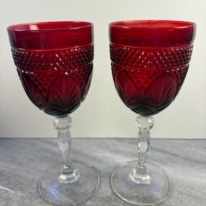 May include: Two ruby red wine glasses with diamond-cut patterns. The glasses have a clear, ornate stem and a round base. The glasses are made of glass and are suitable for serving wine.