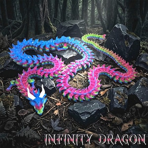 Może przedstawiać: Kolorowa, przegubowa zabawka w kształcie smoka z gradientem niebieskiego, różowego i zielonego. Smok jest ułożony na podłożu z kamieni i liści, z tekstem "INFINITY DRAGON" na dole.