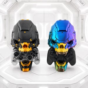 Puede incluir: Dos soportes para mandos de juego con forma de calavera. El soporte izquierdo es negro mate con detalles dorados y sostiene un mando transparente. El derecho tiene un acabado metálico azul y morado con dientes dorados y sostiene un mando negro.