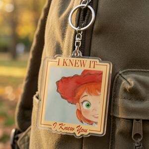 May include: A square acrylic keychain featuring a cartoon illustration of a person with red hair and a red hat. The text I KNEW IT is printed at the top and I Knew You is printed at the bottom in a brown font. The keychain has a silver metal ring.