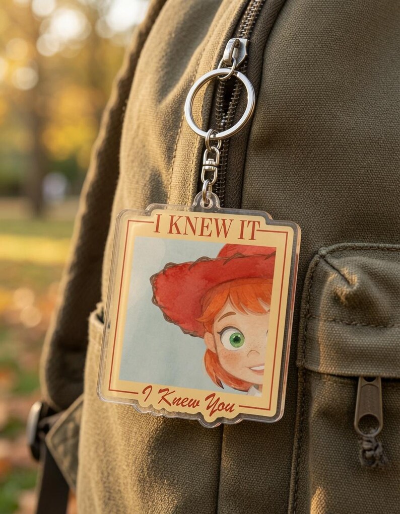 May include: A square acrylic keychain featuring a cartoon illustration of a person with red hair and a red hat. The text I KNEW IT is printed at the top and I Knew You is printed at the bottom in a brown font. The keychain has a silver metal ring.