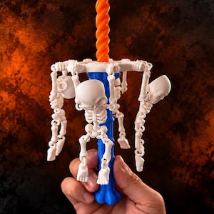 May include: A blue bone-shaped handle supports a circular frame featuring multiple small white articulated skeleton figures hanging from the perimeter, topped with a long orange twisted spiral rod extending vertically from the center.