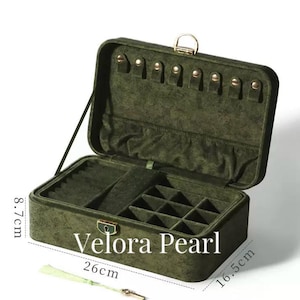 May include: A dark olive green velvet jewelry box with a gold-tone latch and internal compartments. The box measures 26 cm in length, 16.5 cm in width, and 8.7 cm in height. The interior features necklace hooks, a pocket, and grid dividers.
