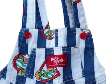 May include: Baby B'gosh blue and white striped overalls with red buttons and a pocket. The overalls feature a repeating pattern of a teddy bear wearing a sailor hat and holding an anchor. The Baby B'gosh label is visible on the pocket.
