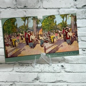 Könnte beinhalten: Eine Vintage-Stereokarte mit einer kolorierten Fotografie einer Dorfszene im Freien mit Menschen in traditioneller Kleidung, Bäumen und Hütten. Der Text am unteren Rand lautet: Animated Scene in a Native Village, Island of Java. Copyrighted, 1903.