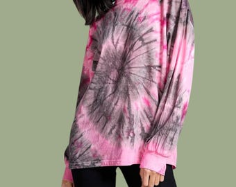 Może przedstawiać: Koszulka z długim rękawem z żywym wzorem tie-dye w odcieniach jaskrawego różu i antracytowej szarości. Wzór rozchodzi się promieniście z centralnego punktu, tworząc efekt koła na całej powierzchni odzieży, w tym na rękawach i przy dekolcie.