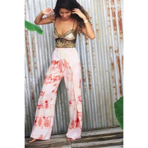 May include: A two-piece outfit comprising a gold and black lace top and light pink tie-dye trousers. The trousers have a wide leg design with red and pink patterns. The top has thin straps and a delicate lace design.