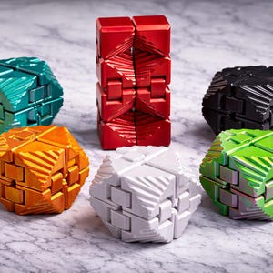 May include: A collection of colorful fidget toys in various shapes. The toys are in shades of red, green, orange, black, and white. The toys are designed with a geometric pattern and are made of a metallic material.