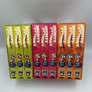 Może przedstawiać: Trzy zestawy pudełek DVD Monty Python's Flying Circus, tomy od 13 do 21. Grzbiety są w kolorze limonkowym, magenty i pomarańczowym, każdy z tytułem programu, numerem tomu i logo A&E na białym tle u podstawy.