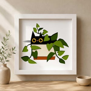 May include: A framed art print featuring a black cat peeking out from a white and brown planter, surrounded by green leaves. The cat has yellow eyes and whiskers. The artwork is set against a white background within a white frame.
