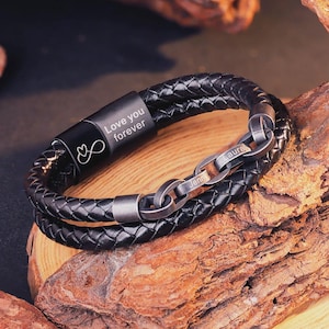 May include: Black braided leather bracelet with a metal clasp. The bracelet features the words "Love you forever" and an infinity symbol engraved on the clasp. The metal clasp also has the names "Jenn" and "Laura" engraved.