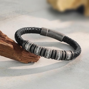 May include: Black braided leather bracelet with silver beads. Each bead is engraved with a name: Aaron, Oakes, Rachel, Madden, and Baber. The bracelet has a magnetic clasp.