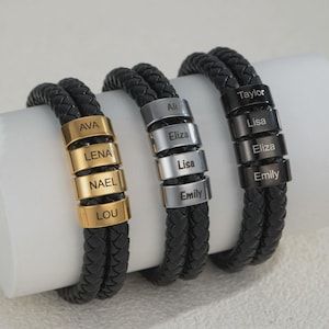 May include: Three black braided leather bracelets with personalized name beads in gold, silver, and black. Each bracelet has multiple beads with names engraved on them. The bracelets are displayed on a white surface.