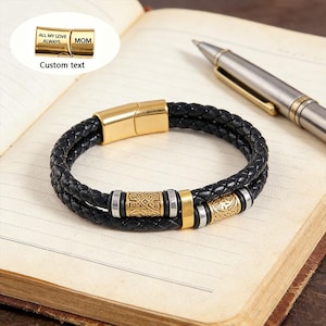 May include: Black braided leather bracelet with gold-colored accents. The bracelet features a gold clasp and decorative gold and silver beads. The text "ALL MY LOVE ALWAYS MOM" is visible on a gold clasp. The words "Custom text" are also visible.