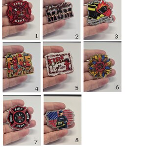 May include: A collection of eight glittery acrylic badges featuring firefighter themes. Designs include a red Maltese cross, the text Firefighter MOM, a fire station scene, a fire hydrant, a sunflower emblem, and an EMS professional with a flag.