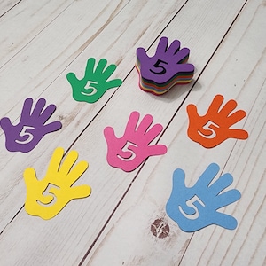 May include: Seven hand-shaped cutouts with the number "5" inside. The cutouts are in different colors: purple, green, orange, pink, yellow, blue, and a stack of multi-colored cutouts.
