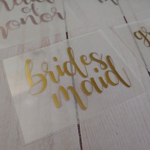 May include: Gold foil lettering on a clear plastic sheet that reads "bridesmaid".