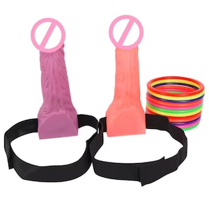 May include: Two dildos, one pink and one orange, with black straps. A stack of colorful rings is also present. The dildos have a textured surface and are designed with a realistic appearance. The black straps are adjustable.