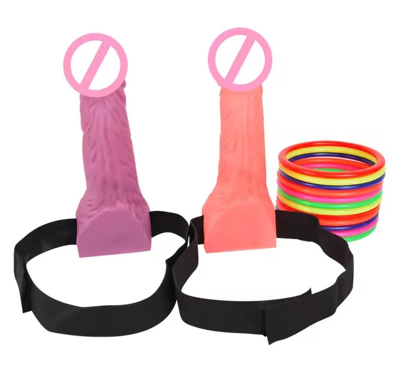 May include: Two dildos, one pink and one orange, with black straps. A stack of colorful rings is also present. The dildos have a textured surface and are designed with a realistic appearance. The black straps are adjustable.
