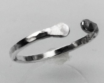 May include: A silver hammered ring with a textured finish. The ring is open and has a slightly curved shape. The ring is marked with the number "925" on the inside.