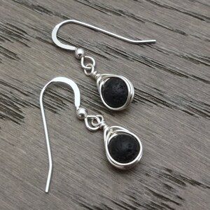 Peut inclure: Une paire de boucles d'oreilles pendantes en argent avec des perles de lave noire. Les perles sont enveloppées de fil d'argent.