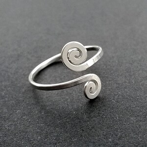 May include: A silver ring with two spiral designs. The ring is open and adjustable.