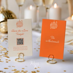 May include: Two rectangular wedding signs held by gold wire stands. The left sign is cream with an orange disco ball icon, the text "Share the Love Tonight," a QR code, and instructions. The right sign is orange with a white disco ball icon and "The Mcdonnells" text.