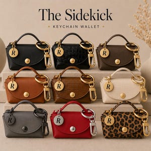 Puede incluir: Nueve carteras llavero en miniatura etiquetadas como The Sidekick, dispuestas en tres filas. Cada una cuenta con un asa superior, un bot&oacute;n a presi&oacute;n dorado o plateado y un dije circular con la letra R. Los colores incluyen negro, marr&oacute;n, tostado, crema, gris, rojo y estampado de leopardo.