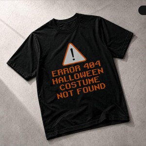 May include: A black short-sleeved t-shirt featuring a graphic of an orange warning triangle with an exclamation point. Below the triangle, the text reads ERROR 404 HALLOWEEN COSTUME NOT FOUND in a pixelated orange font style on the chest area.