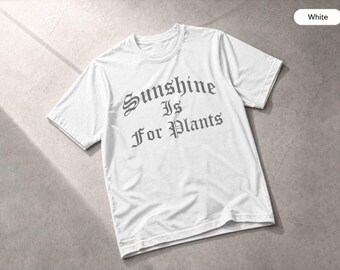 May include: A white short-sleeved t-shirt featuring the text Sunshine Is For Plants printed in a dark grey gothic-style font across the chest. The garment has a crew neckline and a standard fit, showcasing a clean and simple design.