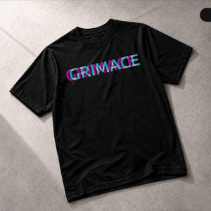 May include: A black short-sleeved t-shirt featuring the word GRIMACE printed across the chest in a layered, glitch-style font with overlapping magenta, cyan, and white colours. The shirt has a crew neckline and a standard fit.